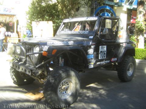 1990 Ford Bronco - black lifted Jeep Wrangler off-road race rig numbered 1706, on large tires with a roll cage and round lights, parked at an event.