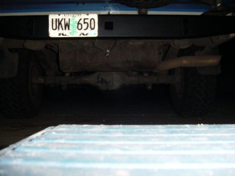 1985 Ford Bronco - The rear underside of a vehicle, showing the axle, exhaust, and a license plate.