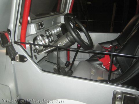 1990 Ford Bronco - Stripped silver off-road vehicle interior with a roll cage, leather steering wheel, gauge cluster and racing bucket seat.