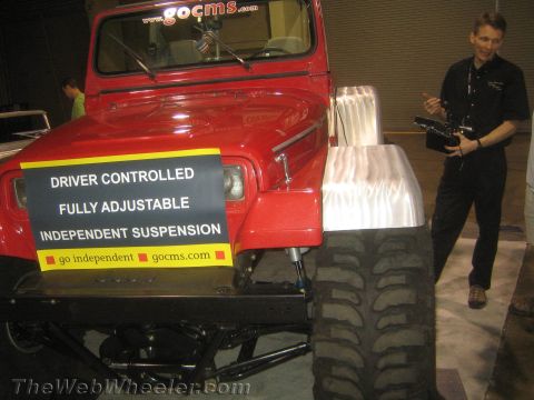 1990 Ford Bronco - Red lifted off-road vehicle displaying a 'Driver Controlled Fully Adjustable Independent Suspension' banner while a man holds a control box.