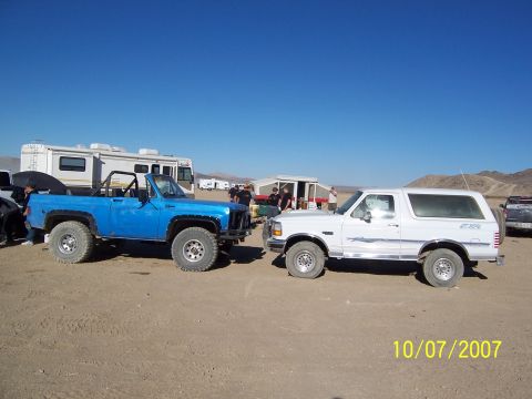 1996 Ford Bronco - A white 1996 Ford Bronco and a blue Chevrolet K5 Blazer are parked side-by-side in a desert setting with RVs in the background.