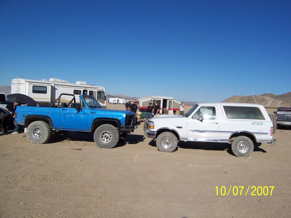 White 1996 Ford Bronco parked next to a blue Chevrolet K5 Blazer in a desert landscape