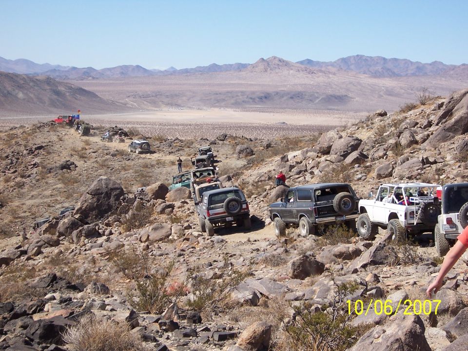 Line of off-road vehicles, including a dark Bronco, driving on a rocky desert trail
