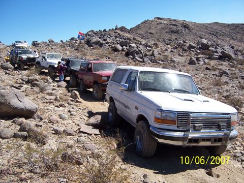 1996 Ford Bronco - A convoy of off-road vehicles navigates a rocky trail under a clear blue sky.