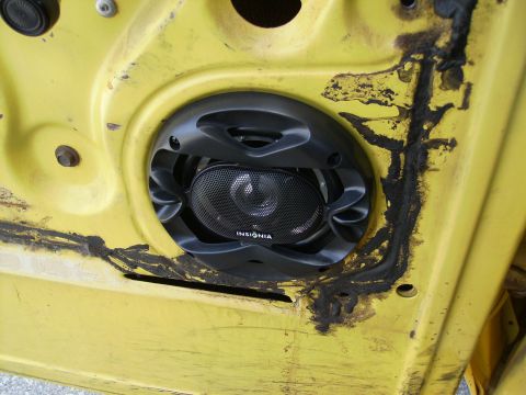 1979 Ford F-100 - An aftermarket speaker is mounted in a yellow car door panel, showing signs of age and modification.