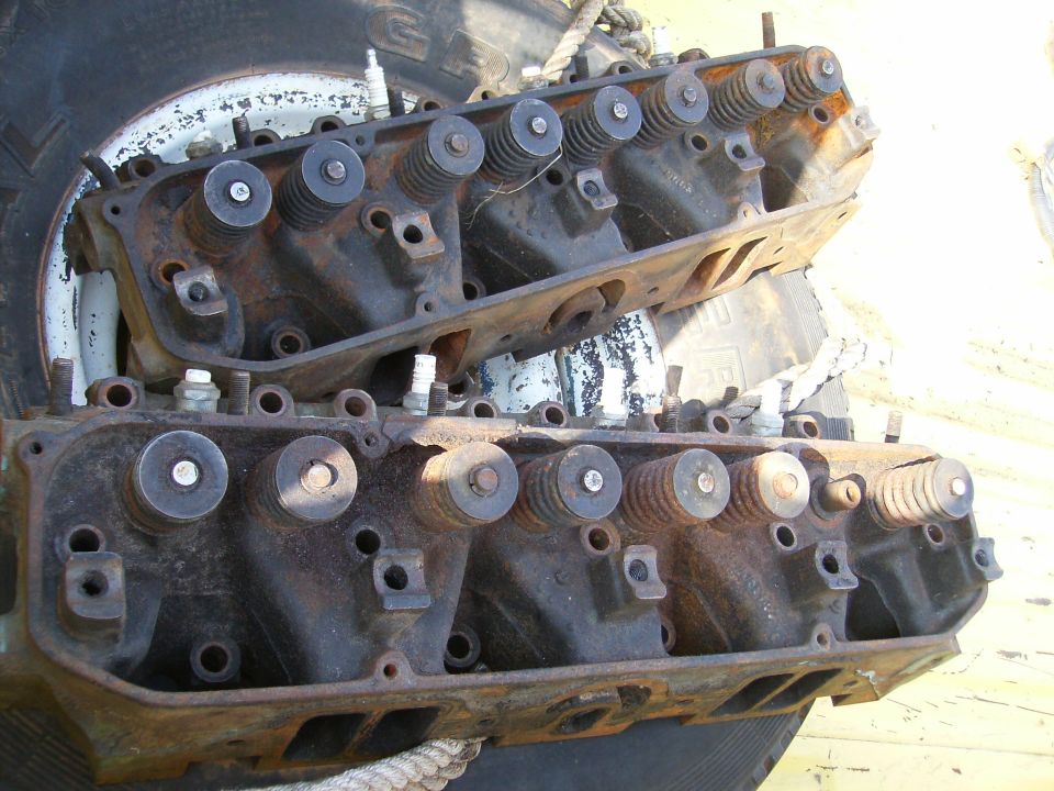 Two rusty engine cylinder heads stacked, showing valve springs and spark plug holes