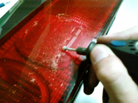 1995 Ford Bronco - A person is cleaning a red car tail light with a rotary tool.