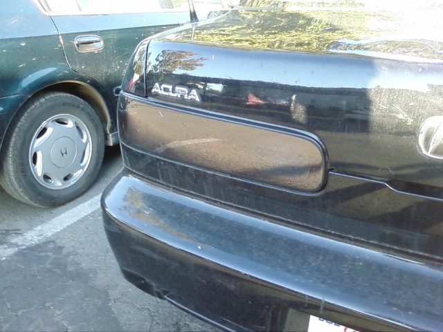 Rear view of a black Acura sedan parked next to a dark green sedan. The Acura has 'ACURA' badging visible