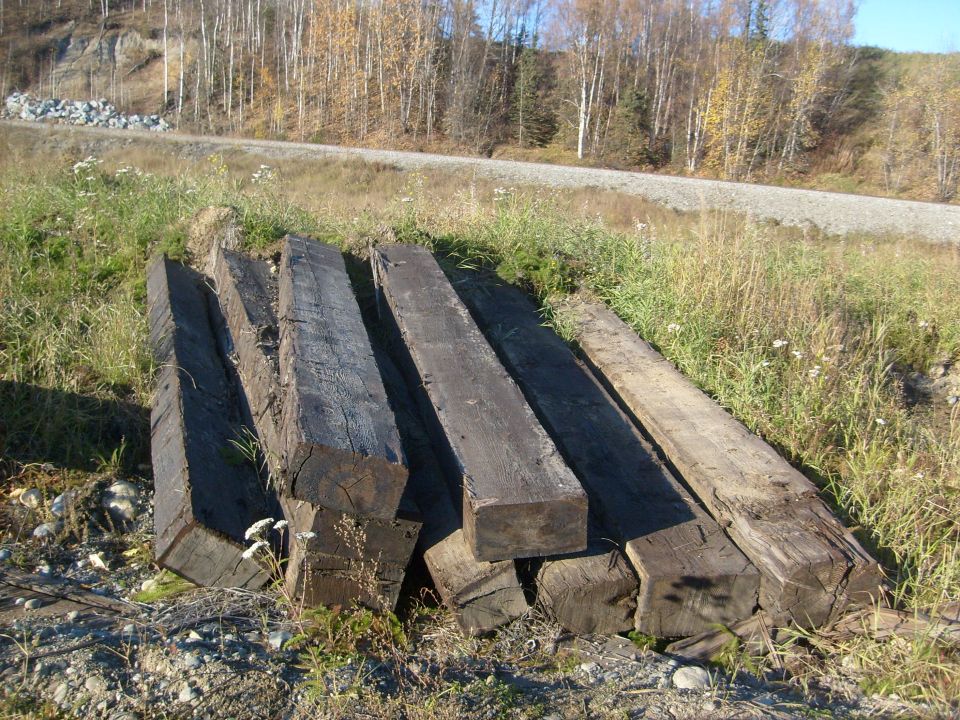 Pile of weathered railroad ties on grassy ground next to a gravel road