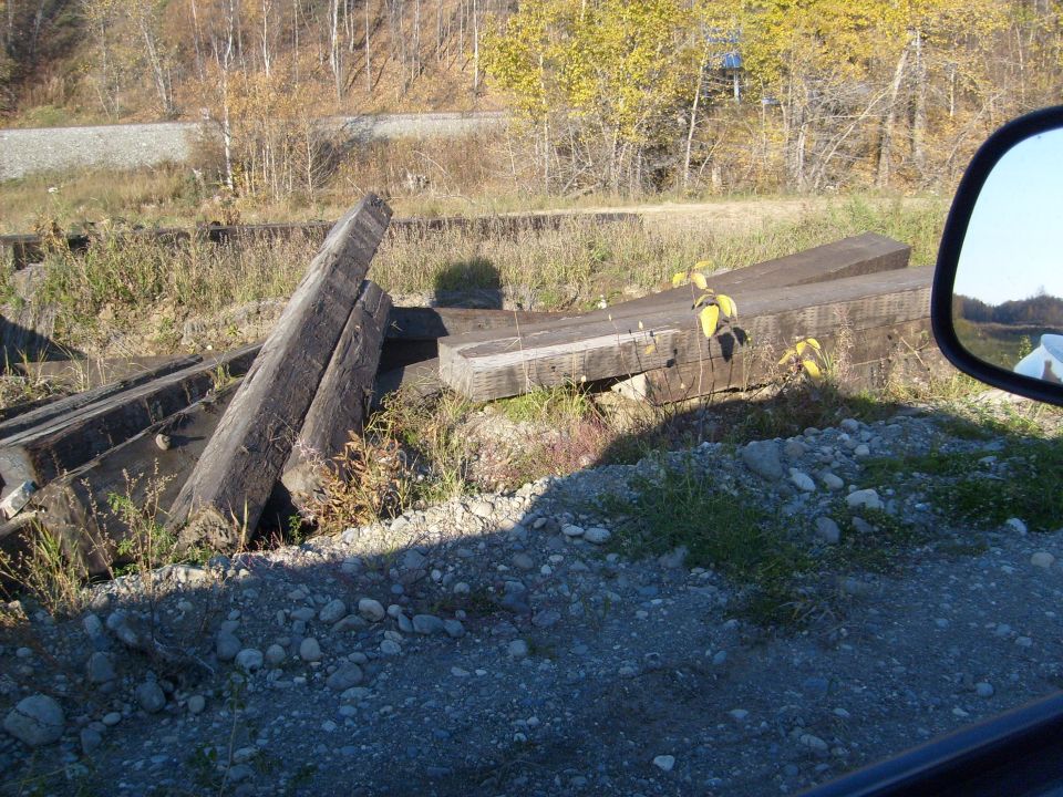 Stacked wooden railroad ties on a gravelly embankment with trees in the background