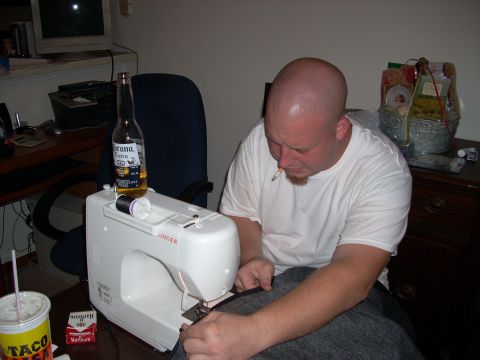 1992 Ford Bronco - A man in a white t-shirt sews grey fabric on a white Singer sewing machine at a desk, with a Corona Extra bottle set on the machine and a T…