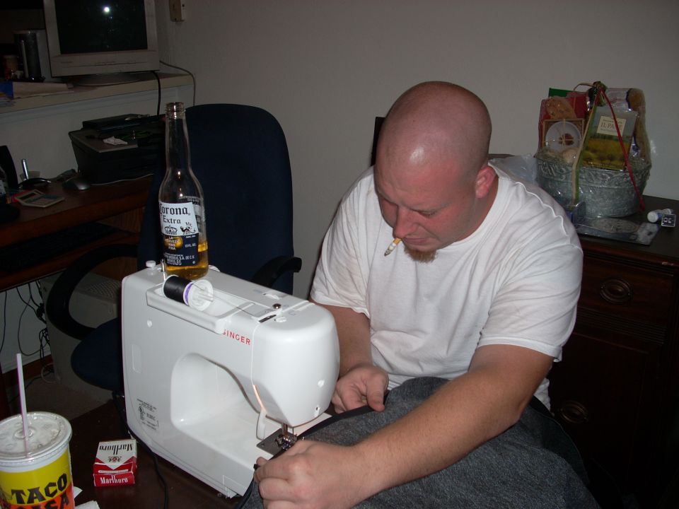 Man sewing grey fabric on a white Singer sewing machine at a desk