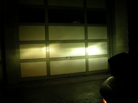 2007 Mazda 3 - Headlights illuminate a garage door, casting bright beams across its panels.