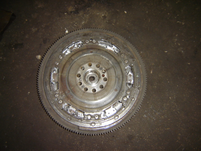 Damaged flywheel with visible wear on clutch surface and broken teeth on outer ring