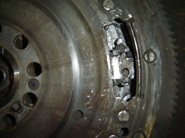 Close-up of a damaged metal flywheel with a large chunk missing and jagged edges