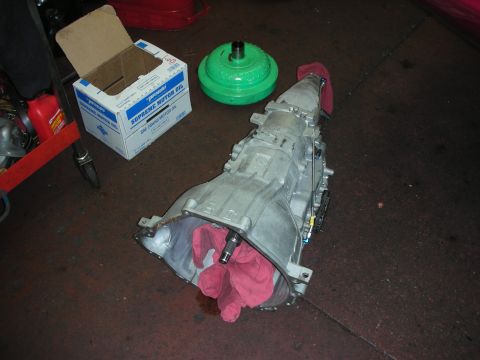 1992 Ford Crown Victoria - A transmission and a green torque converter are shown on a workshop floor, next to a box of Supreme Motor Oil.