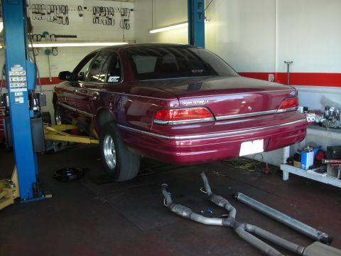 1992 Ford Crown Victoria - Maroon 1992 Ford Crown Victoria LX undergoing service in a workshop, new exhaust components laid out nearby.