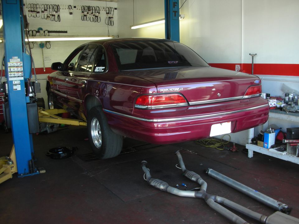 1992 Ford Crown Victoria LX on a lift in a garage, with exhaust parts on the floor
