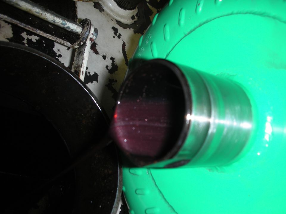 Close-up of dark red fluid in a metal pipe, with a green circular object in the background