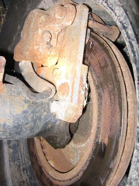1989 Ford Bronco - Close-up view of a heavily rusted brake caliper and rotor, indicating significant wear and age.