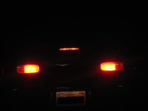 1995 Ford Bronco - The rear of a vehicle is visible at night, with its taillights illuminated and a California license plate attached.