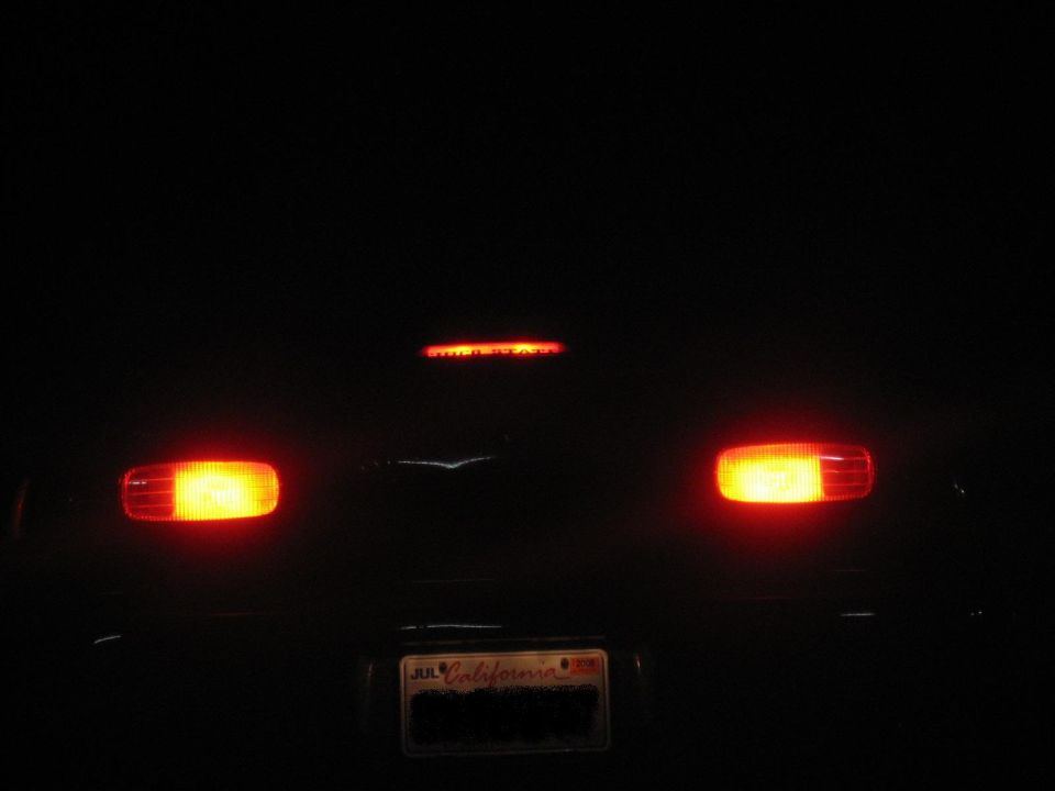 Rear of a dark vehicle with illuminated taillights and a California license plate