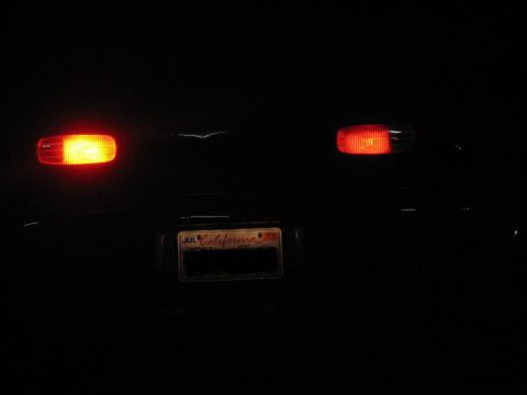 1995 Ford Bronco - The rear of a dark SUV is visible at night, illuminated tail lights and a California license plate.