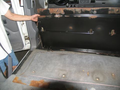1995 Ford C-350 (Centurion Conversions) - The interior of a van is shown with a panel being held up, revealing the floor and dashboard area.