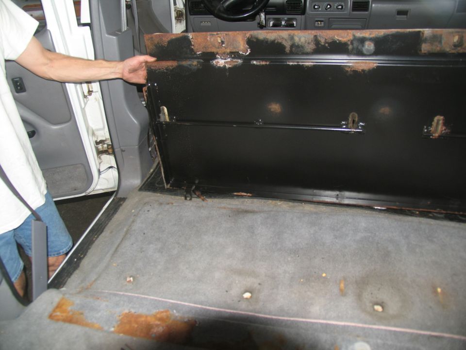 Person's hand holding up a panel inside a van, showing the interior floor and dashboard
