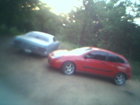 1973 Mercury Monterey - Two vehicles, a red hatchback and a light blue sedan, are parked on a dirt road surrounded by trees.
