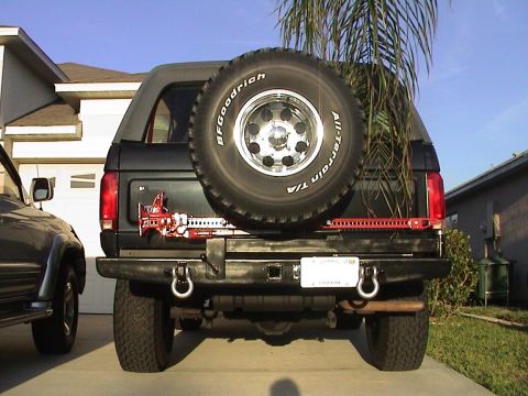 1979 Ford Bronco - Rear view of a 1979 Ford Bronco, equipped with a spare tire and Hi-Lift jack, parked next to another vehicle.