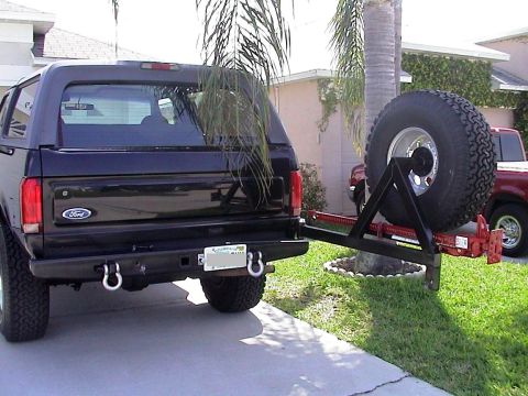 1979 Ford Bronco - The rear of a black Ford Bronco is shown with a spare tire mounted on a swing-away carrier, with another vehicle visible in the background.