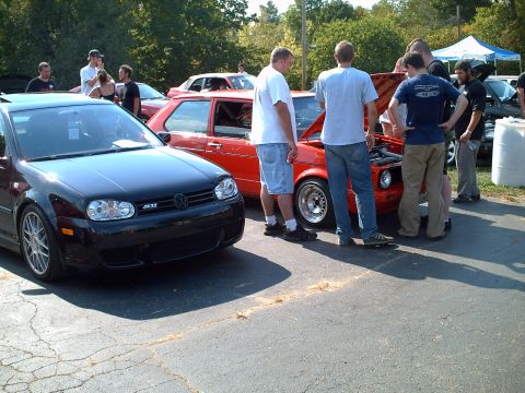 2003 Volvo S40 - A group of people gather around a red Volkswagen Golf GTI with its hood open, while a black Volkswagen Golf GTI is parked in the foreground.
