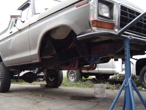 1978 Ford Bronco - The front end of a silver 1978 Ford Bronco is elevated on a blue jack stand, revealing its suspension and exhaust system.