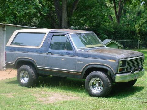 1984 Ford Bronco - This Ford Bronco is parked on a grassy area next to a building and trees.