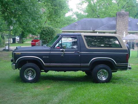 1984 Ford Bronco - This dark blue 1984 Ford Bronco features a tan removable top and is parked on a grassy lawn.