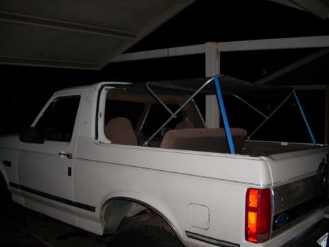 1992 Ford Bronco - White 1992 Ford Bronco photographed at night from the passenger side, with the doors and roof removed and a soft-top frame installed over t…