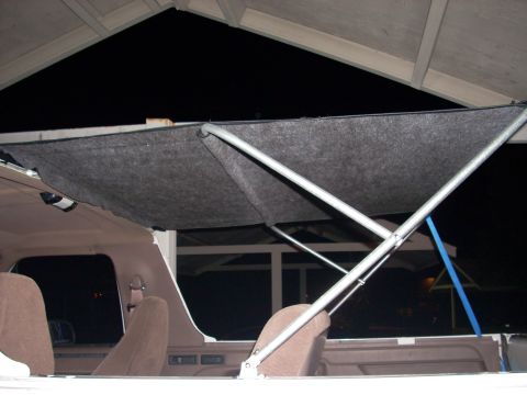 1992 Ford Bronco - View from inside an open-cab truck at night showing a tubular metal soft-top frame covered with gray felt-like liner material stretched ove…