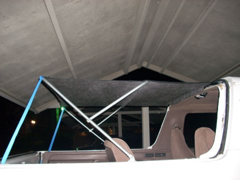 1992 Ford Bronco - Night shot of a bimini-style soft top being fitted to the rear of a white truck/SUV with the hardtop removed, showing the crossed silver tu…