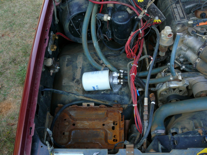 Engine bay showing a white fuel filter, rusty battery tray, and wiring