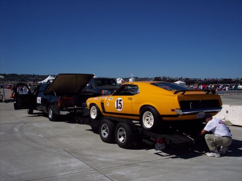1971 Ford Mustang - A yellow race car is being loaded onto a trailer by a man, with a black truck nearby.