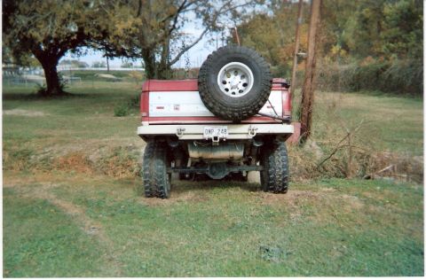 1995 Ford Bronco - This red and white SUV is seen from the rear, a spare tire mounted externally and a visible license plate.