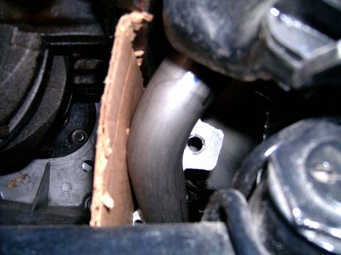 1978 Ford Mustang II - A close-up view of an exhaust pipe and surrounding engine components, with a piece of cardboard for protection.