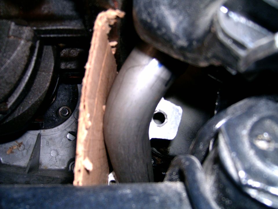 close-up of an exhaust pipe near engine parts, with a piece of cardboard