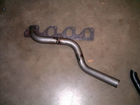 1978 Ford Mustang II - A set of exhaust headers and a gasket lie on a concrete floor, likely for a vehicle repair or upgrade.