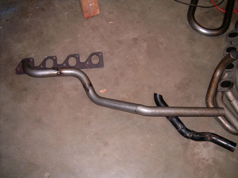 Exhaust manifold with gasket and bent pipe section, next to other exhaust pipes