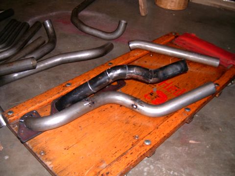 1978 Ford Mustang II - Various exhaust pipes are laid out on a wooden cart, some showing signs of welding and wear.