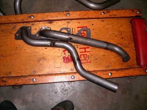1978 Ford Mustang II - Custom exhaust headers are shown resting on a wooden surface. Partial text 'Hed' is visible on the surface.