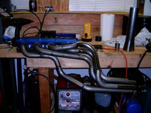 1978 Ford Mustang II - Engine headers and a blue engine block sit on a workbench, alongside welding equipment and tools.
