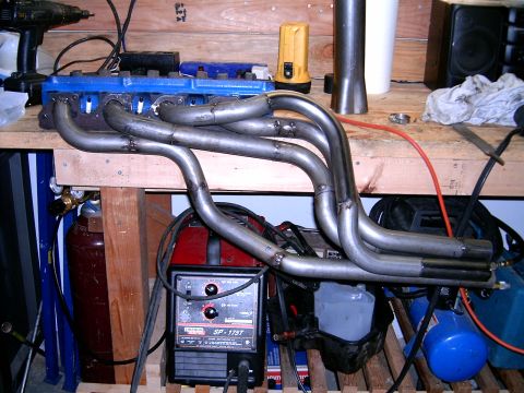 1978 Ford Mustang II - Custom exhaust headers sit on a workbench next to welding equipment and an air compressor.
